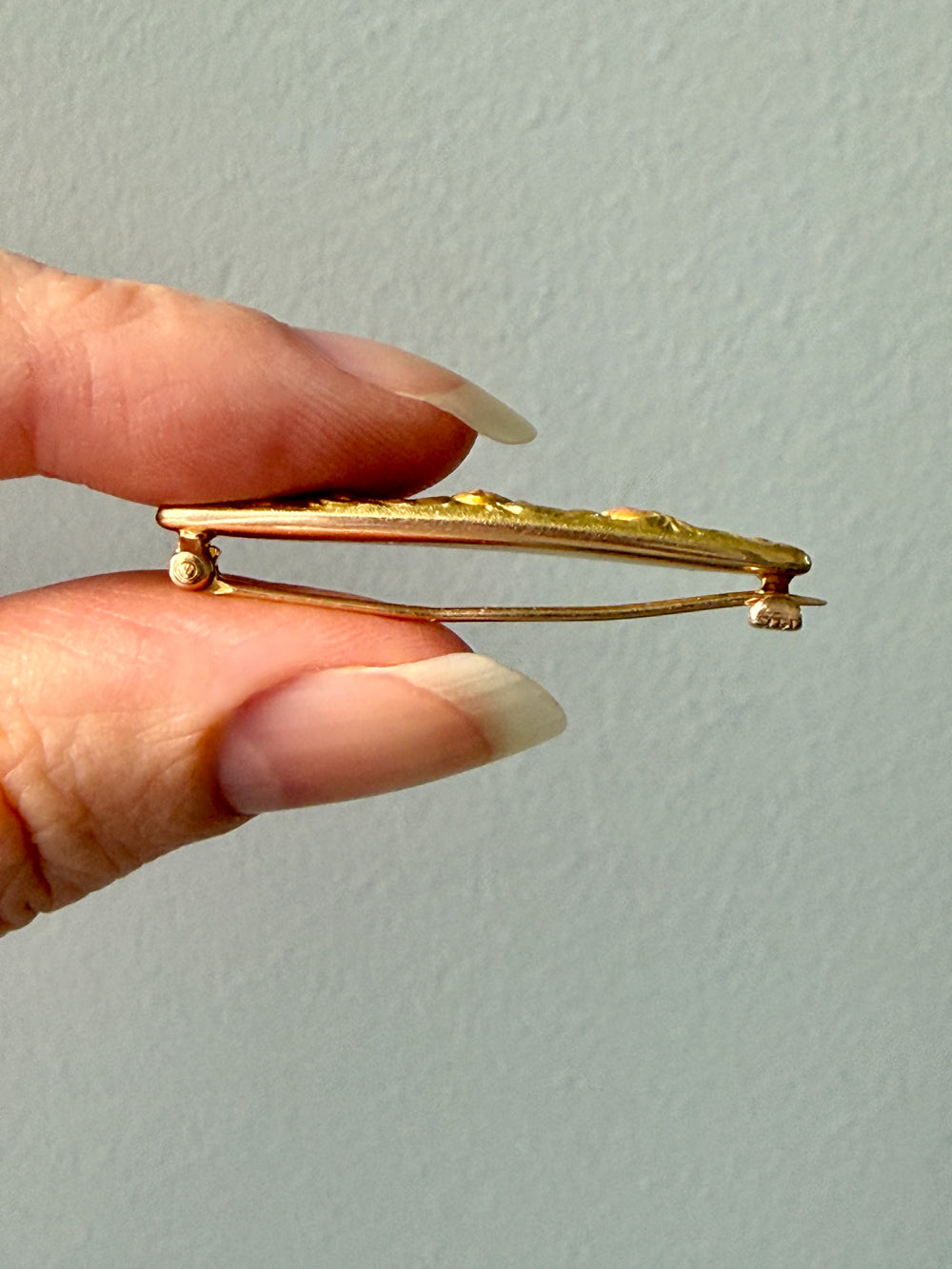 Gold brooch held by a hand against a light gray background