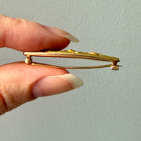 Gold brooch held by a hand against a light gray background