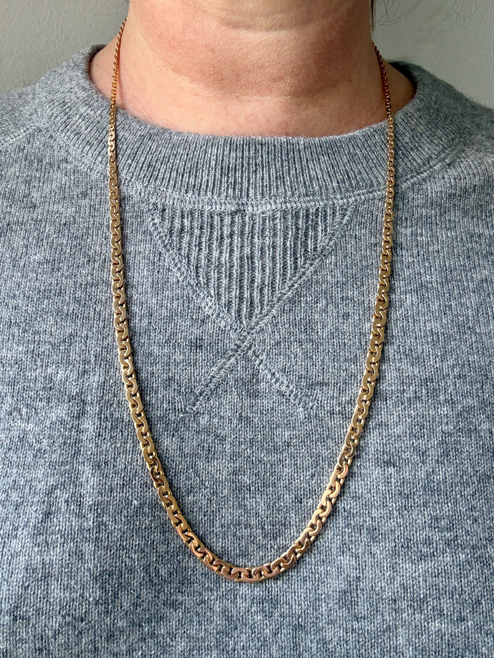 Gold chain necklace on a person wearing a gray sweater