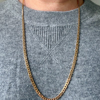 Gold chain necklace on a person wearing a gray sweater