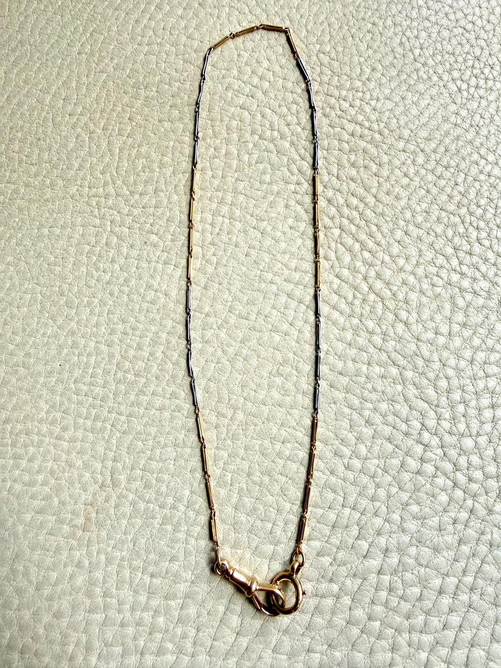 18k Gold and platinum watch chain with clip on a textured beige background