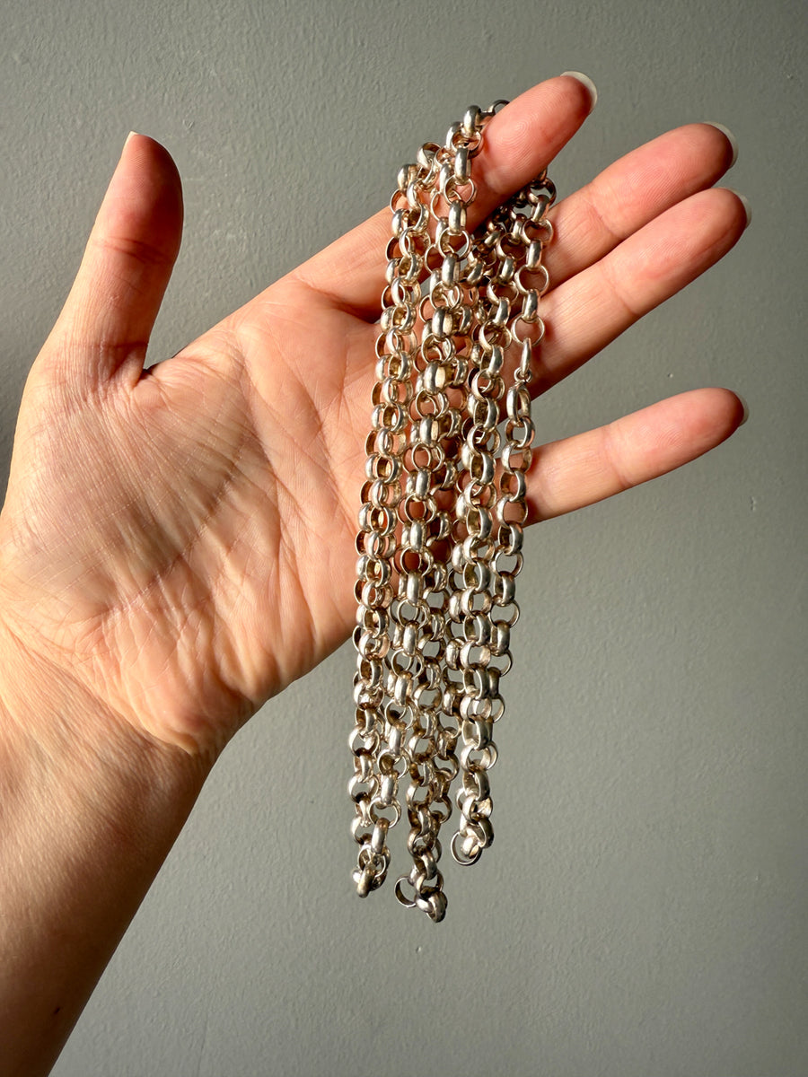 Hand holding a long silver chain against a neutral background