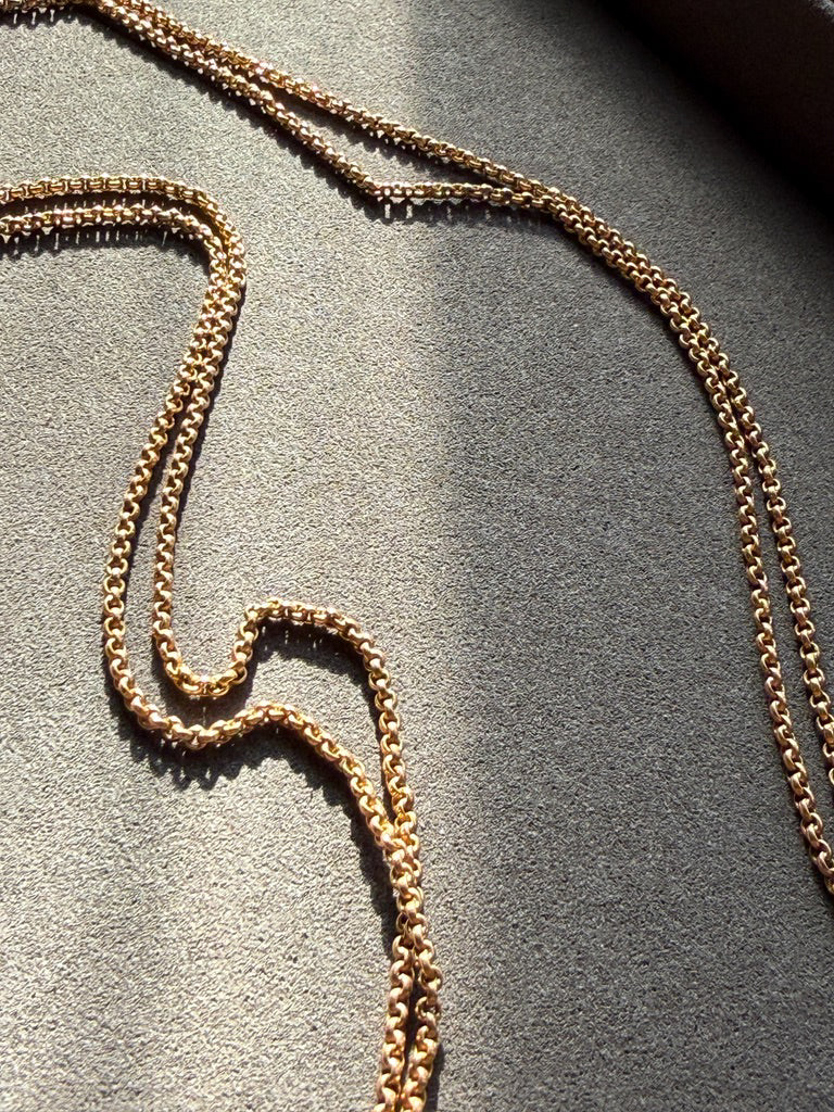 Gold rolo chain necklace on a textured gray surface