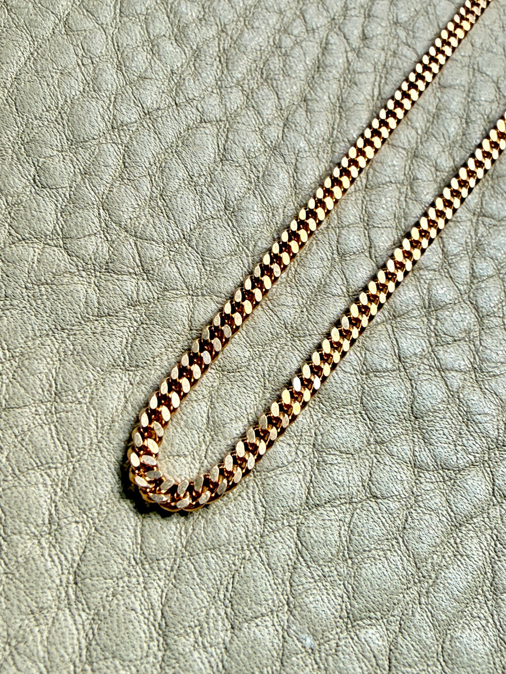 18k Gold curb chain necklace on a textured light surface