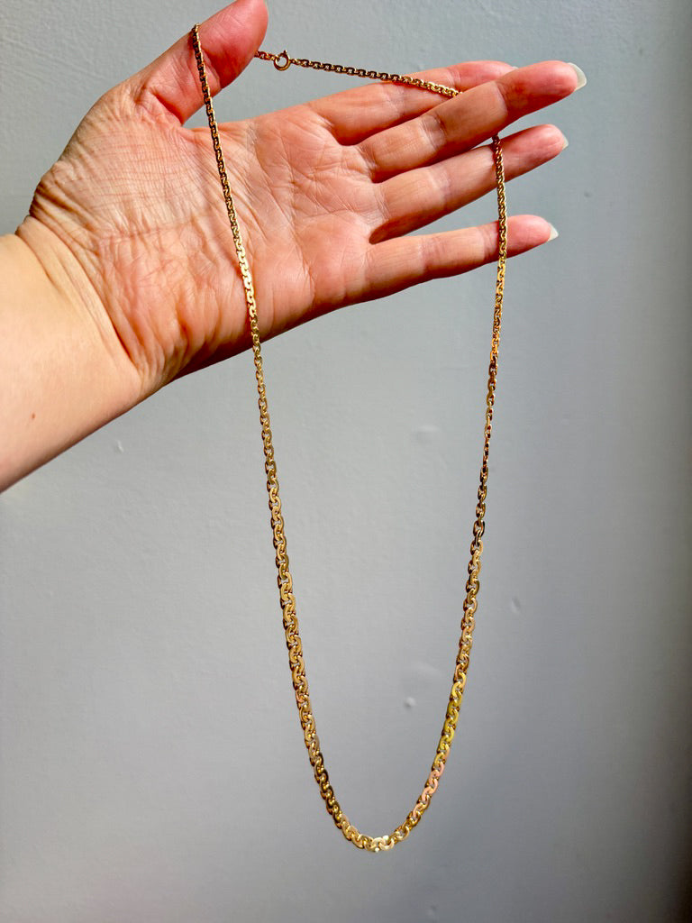 Gold chain held by a hand against a gray background