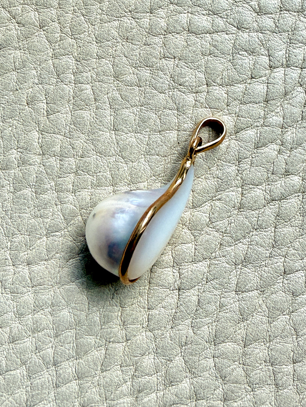 Pearl pendant with gold setting on a textured light gray background