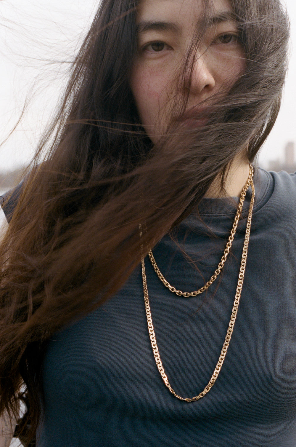 Woman with long hair and gold chain necklaces against a blurred background