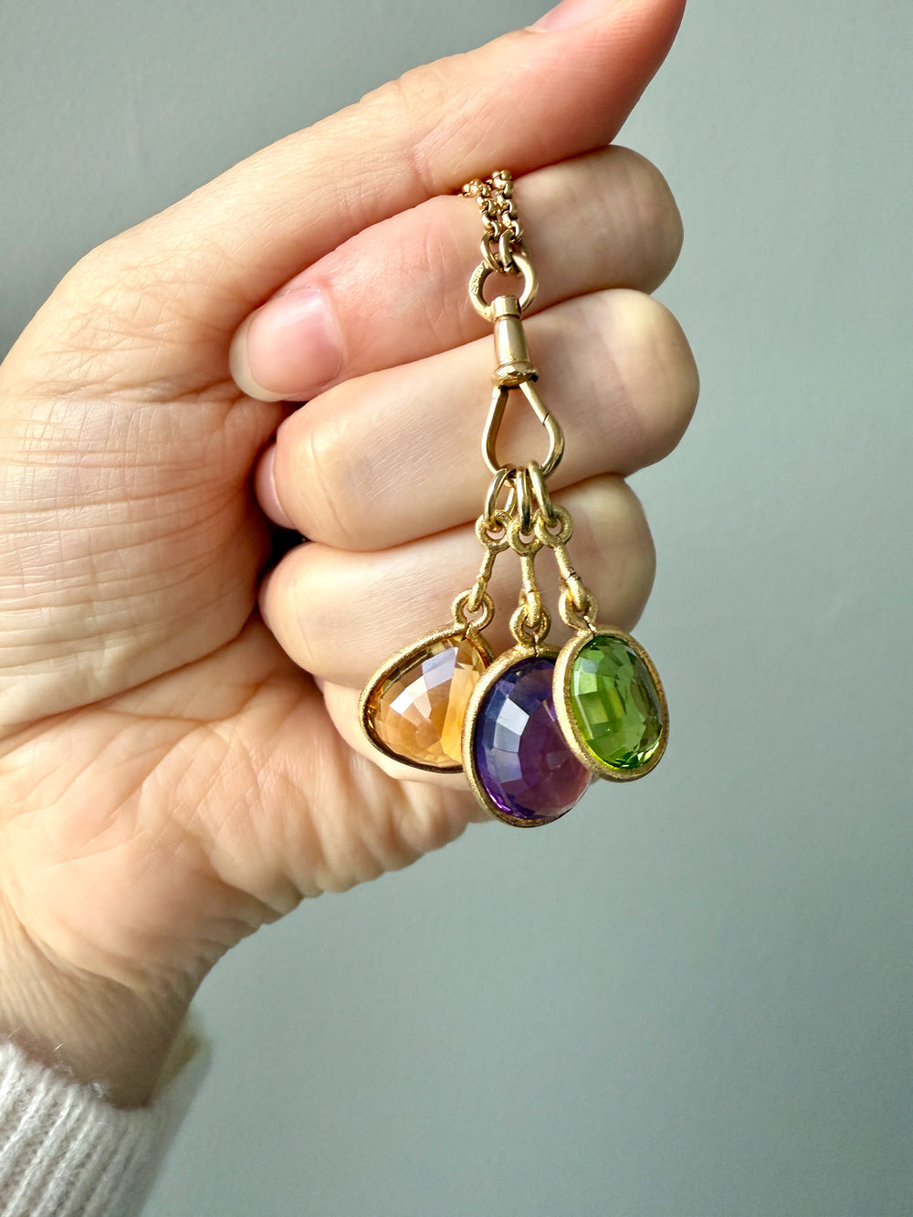 Gold necklace with multicolored gemstones held by a hand against a neutral background