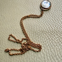Necklace with a round pendant on a textured beige surface. Penelope Penelope vintage gold jewelry