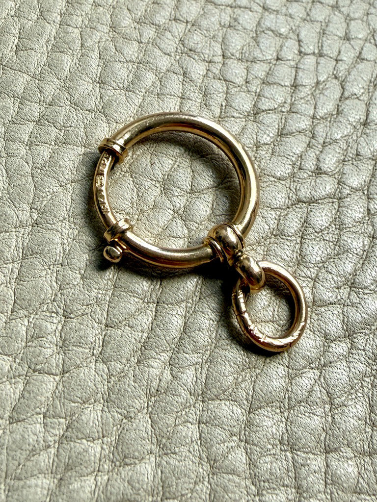 18k Gold antique bolt ring jewelry clasp piece on a textured light gray background