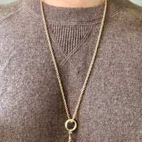 Gold necklace with a purple pendant worn by a person in a brown sweater.