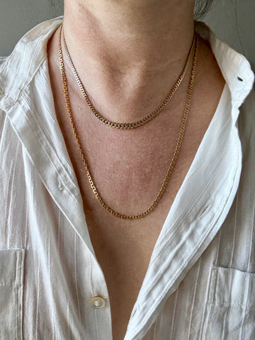 Person wearing a gold chain necklace with a white shirt.