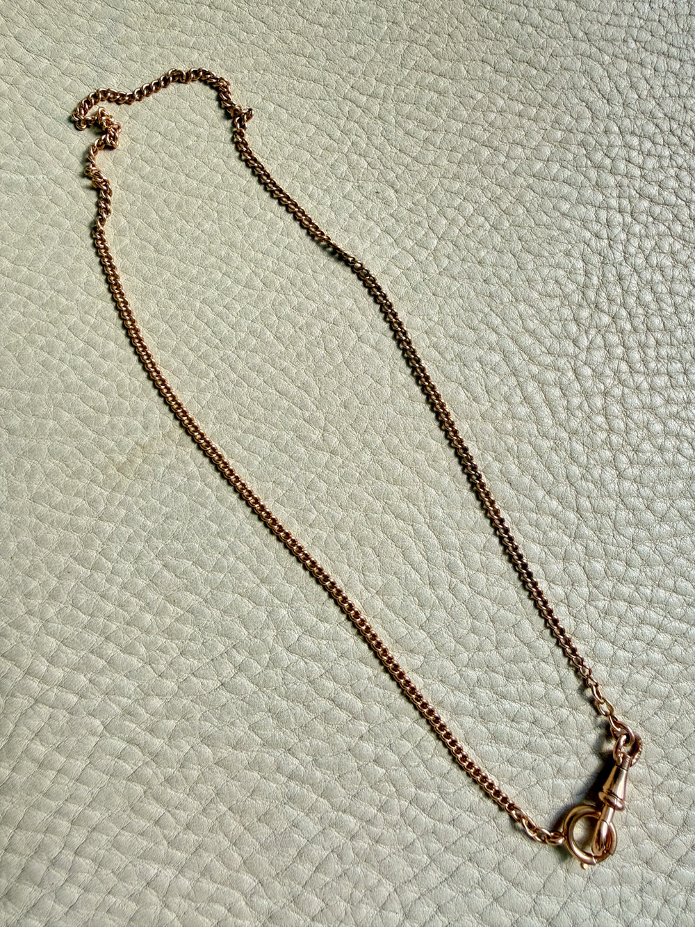 Gold necklace with a clasp on a textured light green surface