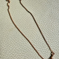 Gold necklace with a clasp on a textured light green surface