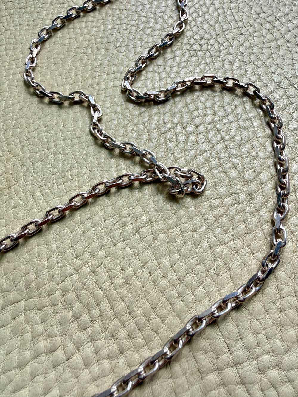 Silver chain necklace on a textured green surface