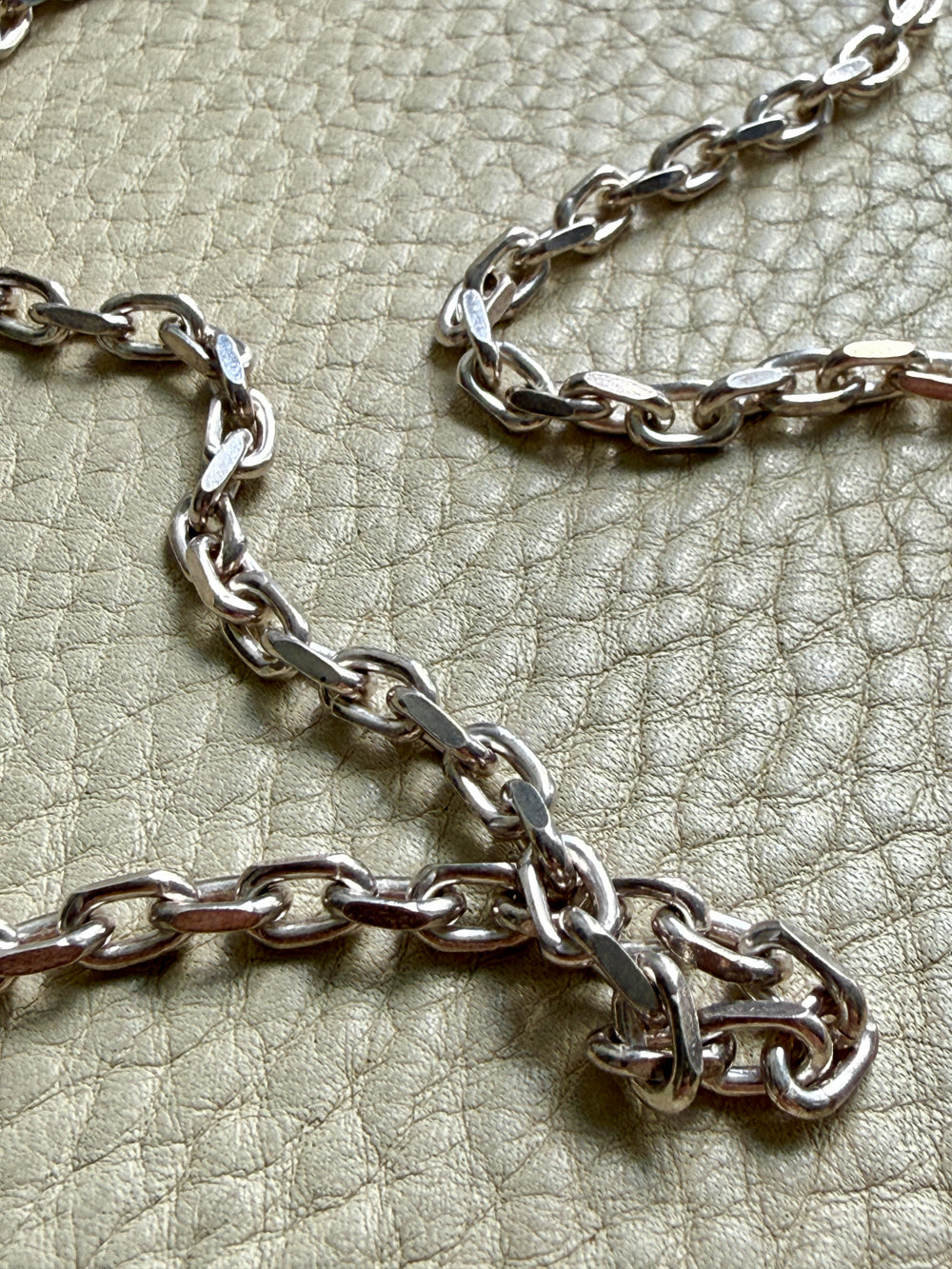Close-up of a silver chain on a textured beige surface