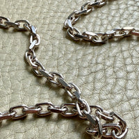 Close-up of a silver chain on a textured beige surface