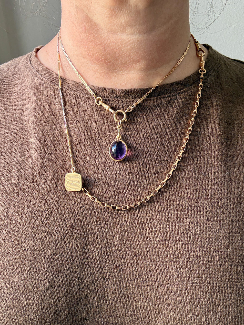Gold necklace with a pendant worn by a person on a plain background