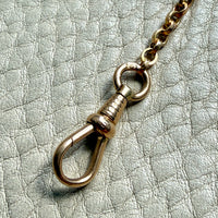 antique 18k Gold watch chain with dog clip on a textured light gray background