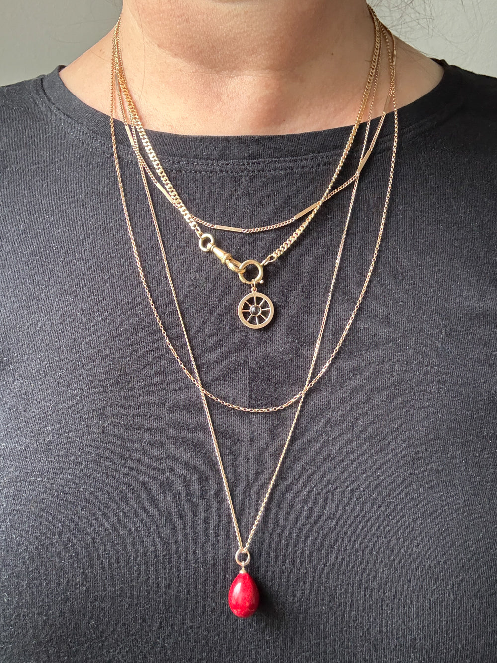 Person wearing multiple vintage 18k gold necklaces with a red pendant on a plain background penelopepenelope.com