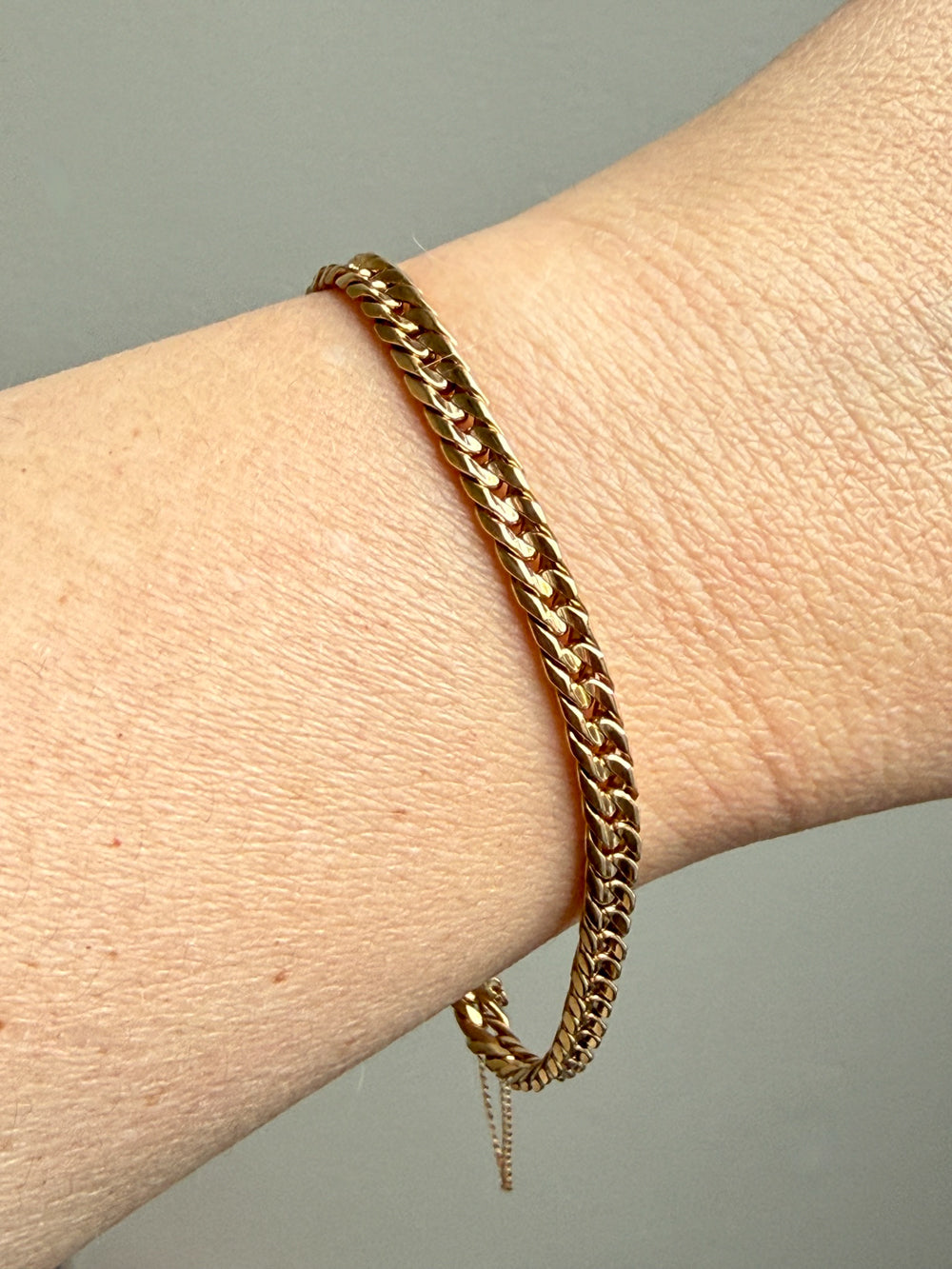 Gold chain bracelet on a wrist against a neutral background