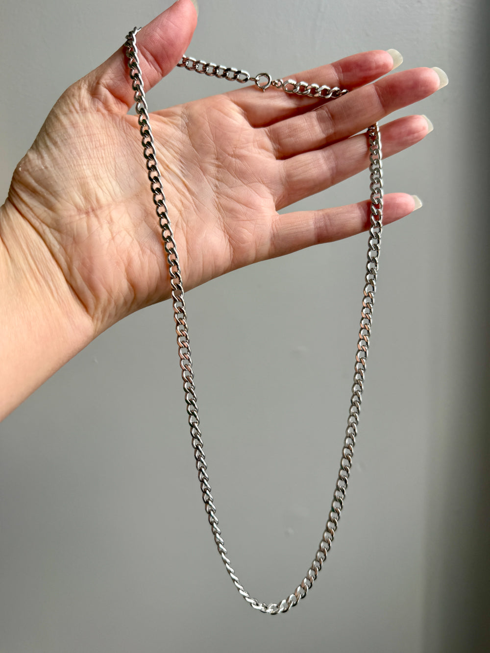 Hand holding a vintage 14k white gold chain  chain against a gray background