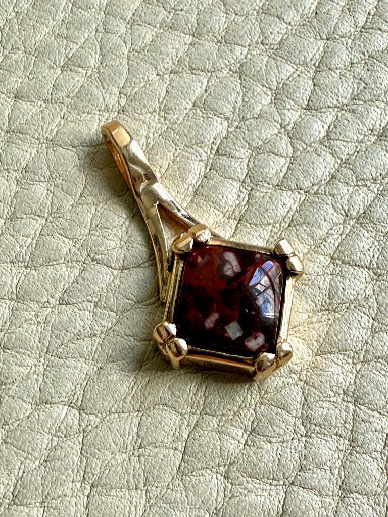 Gold pendant with a red gemstone on a textured light gray background