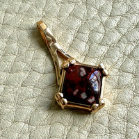 Gold pendant with a red gemstone on a textured light gray background