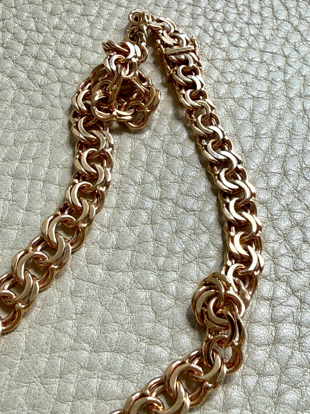 A close-up of a chunky 18k gold chain necklace laid on a textured off-white surface.