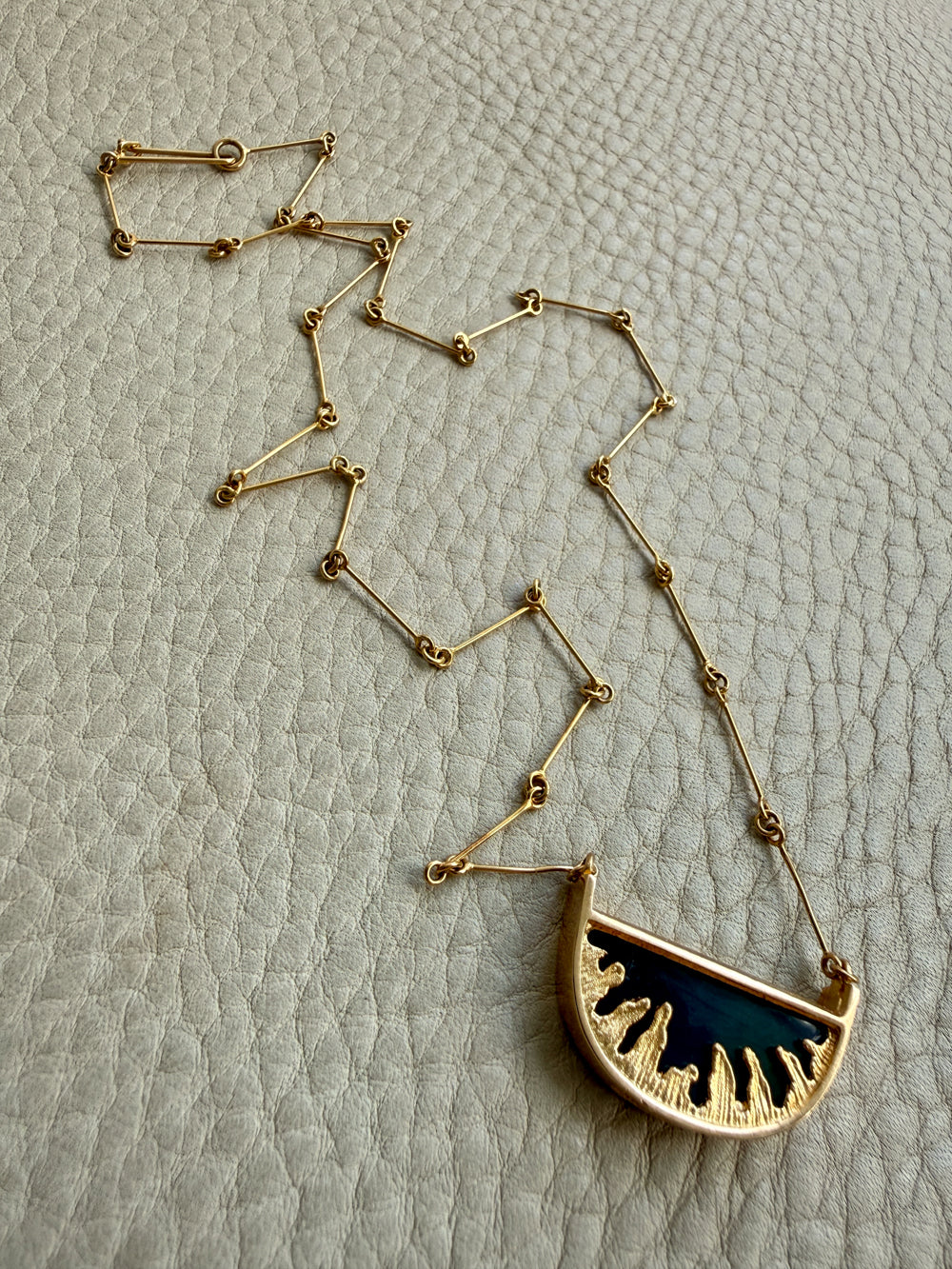 Gold necklace with a half-moon pendant on a textured beige background
