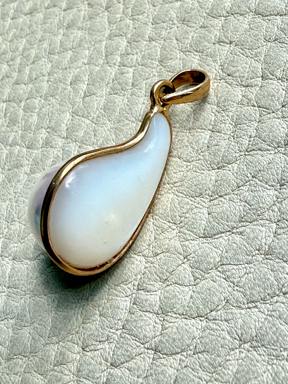 Teardrop-shaped pearl pendant with gold rim on a light gray textured background