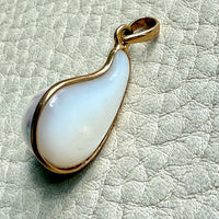 Teardrop-shaped pearl pendant with gold rim on a light gray textured background