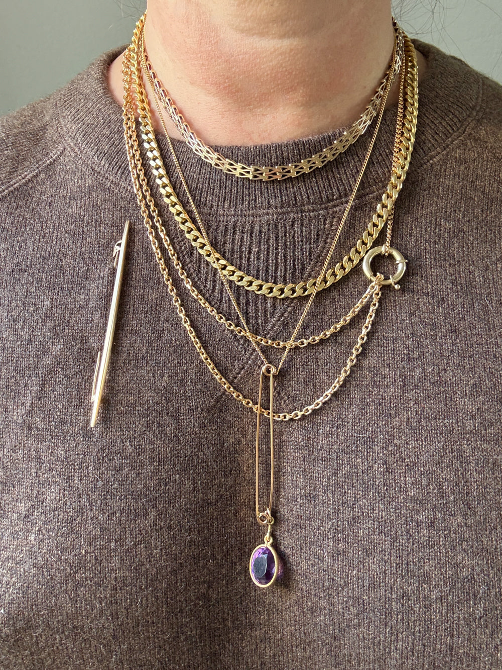 Person wearing multiple gold necklaces with a brooch on a gray background
