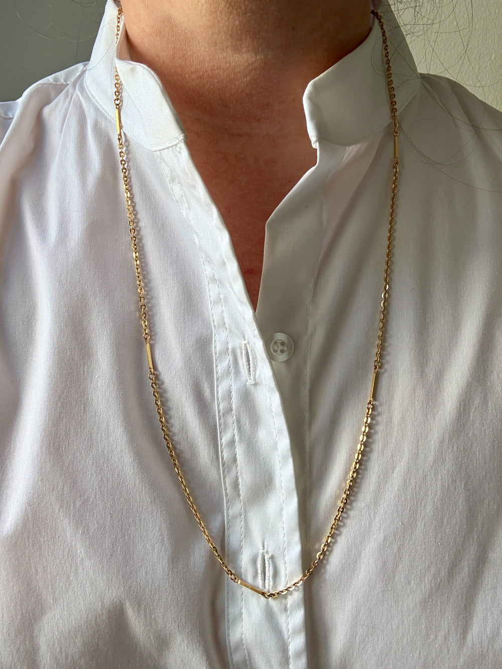 Gold chain necklace worn by a person in a white shirt.