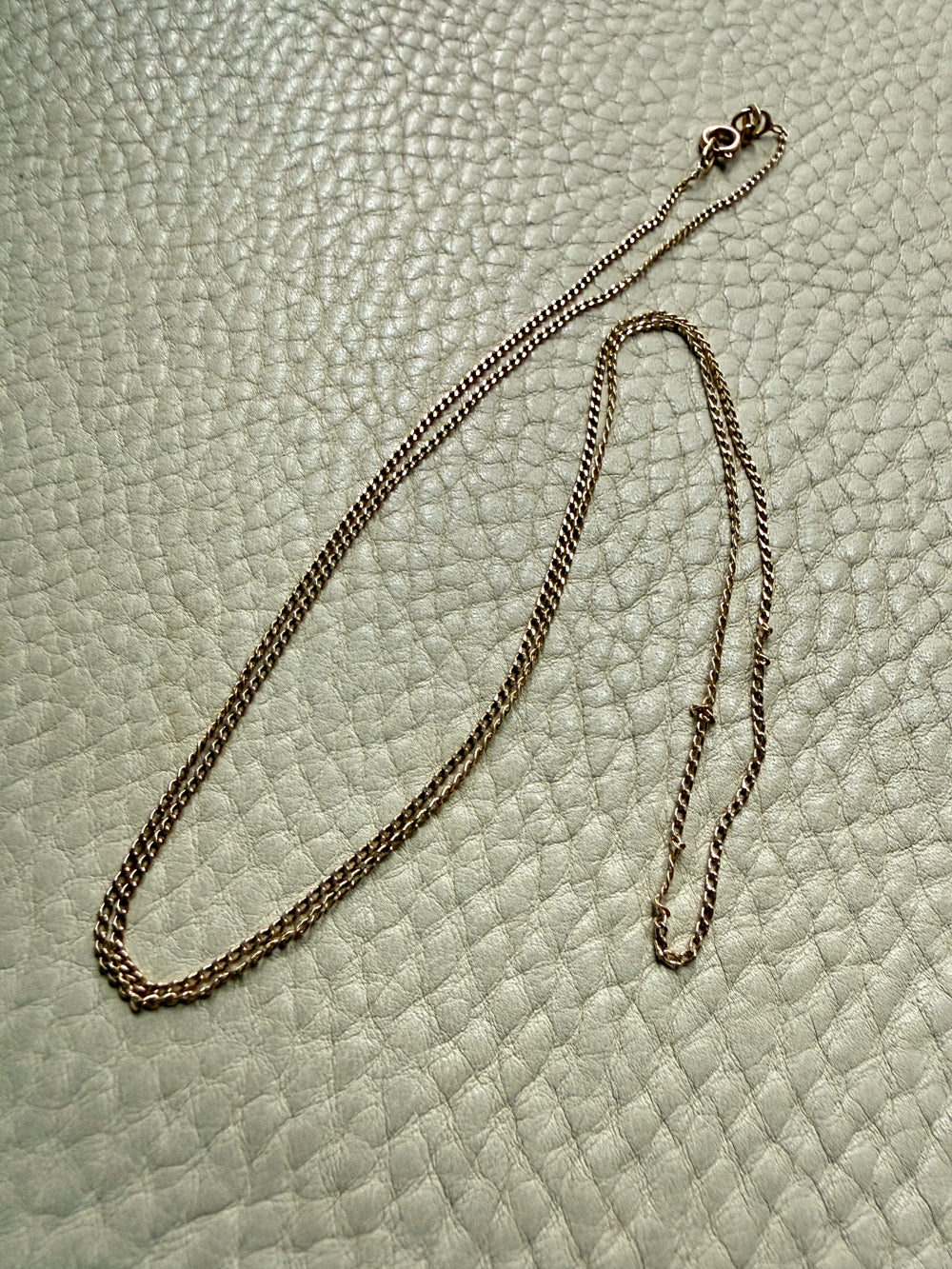 18k gold curb link necklace on a textured light green surface