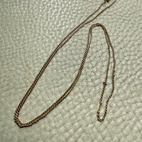 18k gold curb link necklace on a textured light green surface