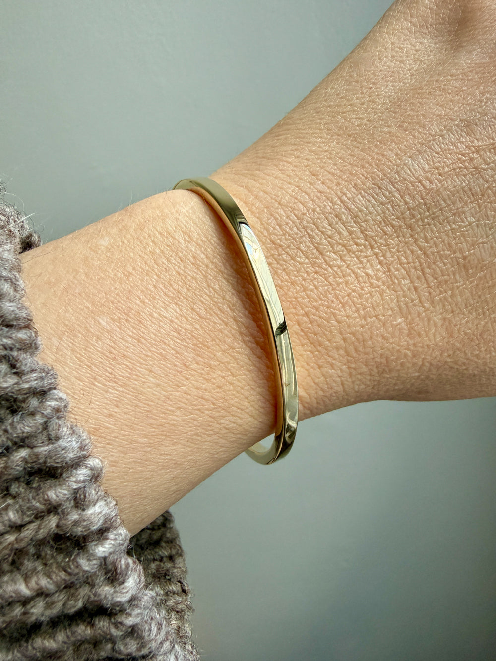 14k Gold solid bangle bracelet on a wrist with a neutral background