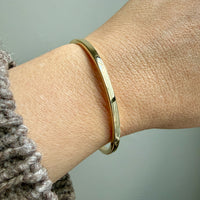 14k Gold solid bangle bracelet on a wrist with a neutral background