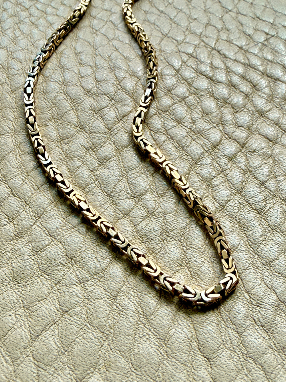 14k gold Gold byzantine chain necklace on a textured beige surface penelopepenelope.com fine jewelry