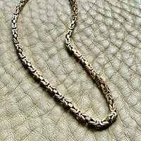 14k gold Gold byzantine chain necklace on a textured beige surface penelopepenelope.com fine jewelry