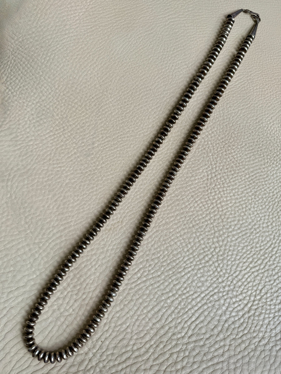 Necklace with silver beads on a textured beige surface