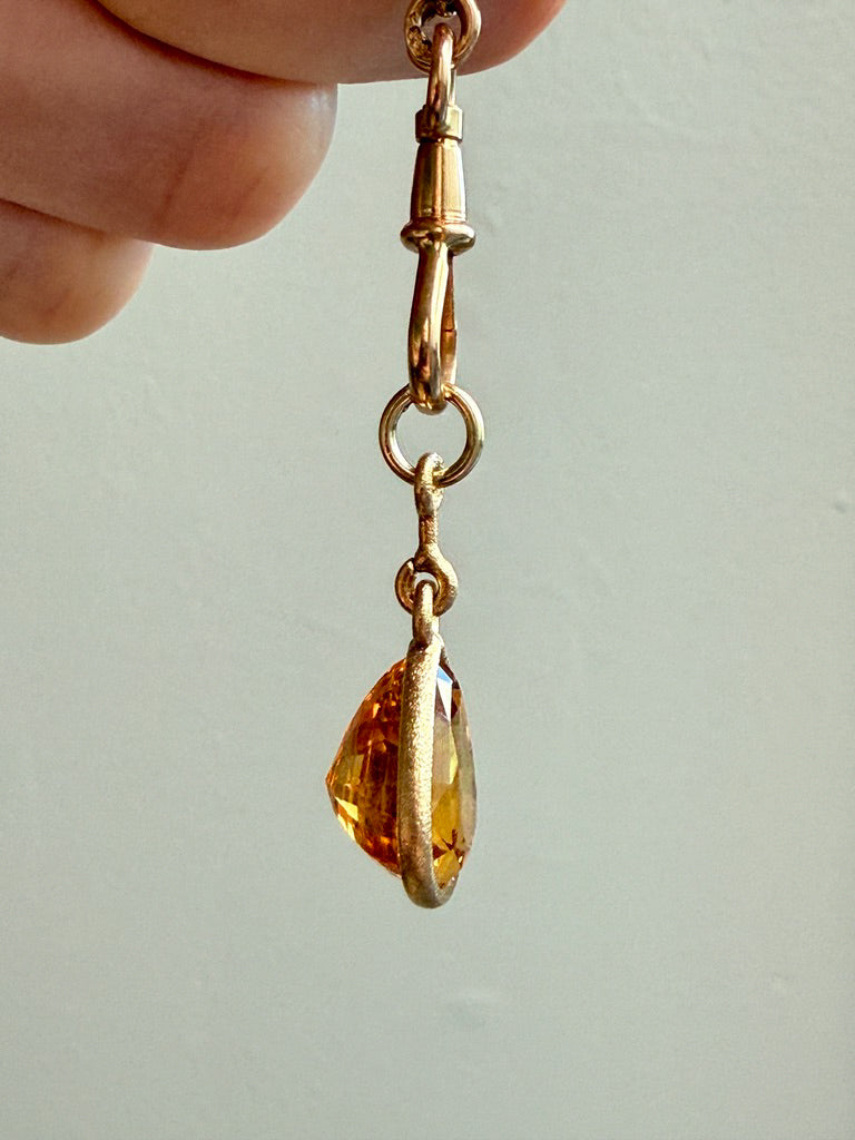 Gold earring with a teardrop-shaped amber stone held by a hand against a light background