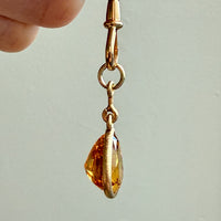 Gold earring with a teardrop-shaped amber stone held by a hand against a light background