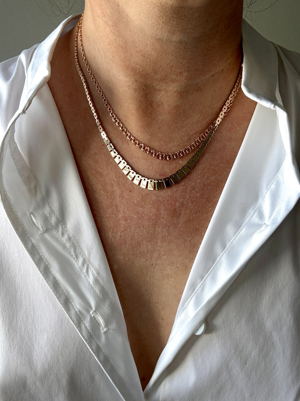 Close-up of a person wearing two gold necklaces with a white shirt.