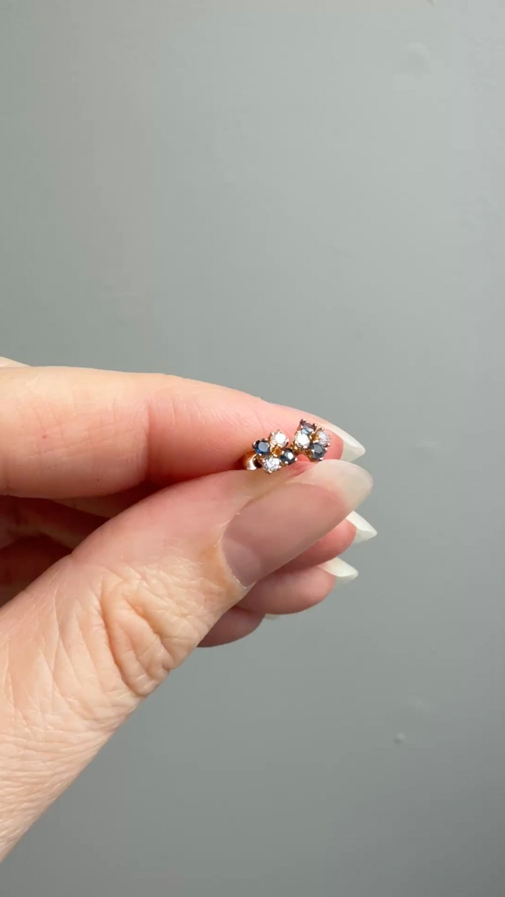 Hand holding a small earring with a gray background