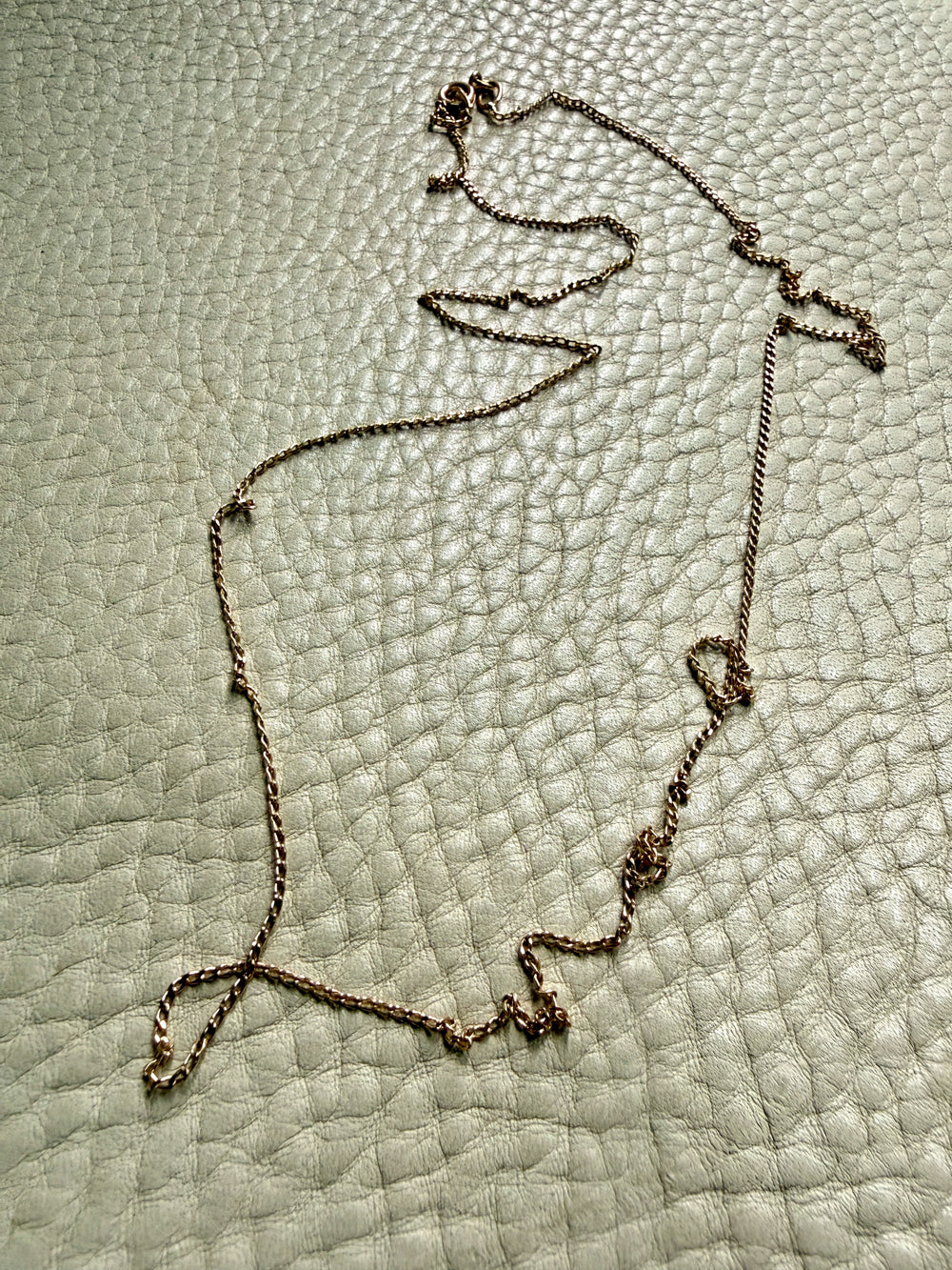 18k gold curb link Necklace on a textured light green surface