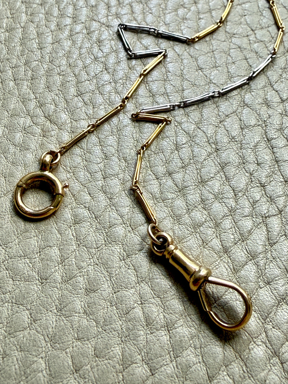 18k Gold and platinum watch chain with clip on a textured beige background