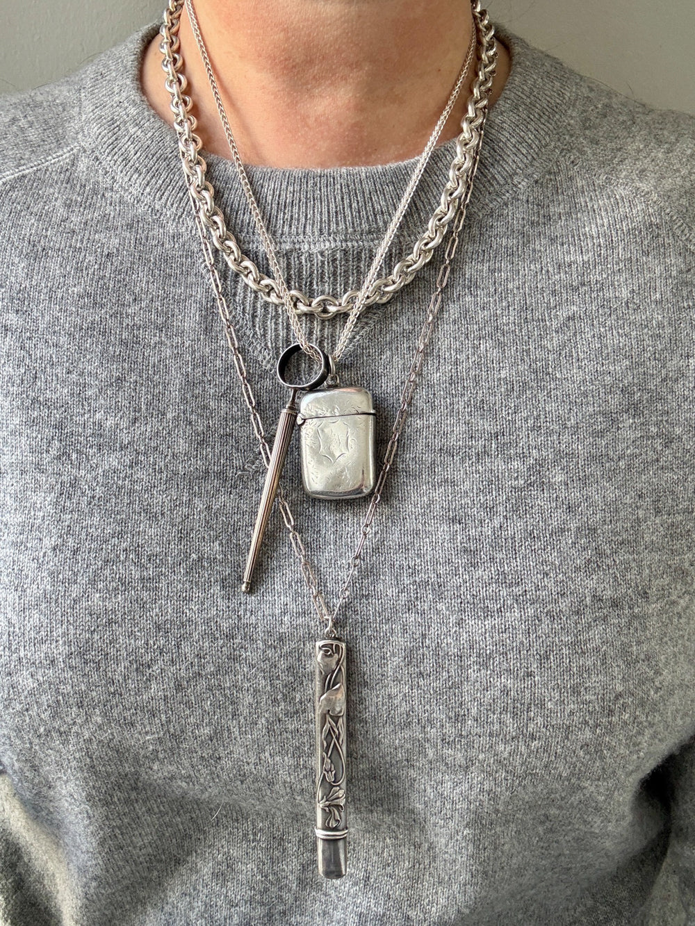 Person wearing a gray sweater with layered silver necklaces