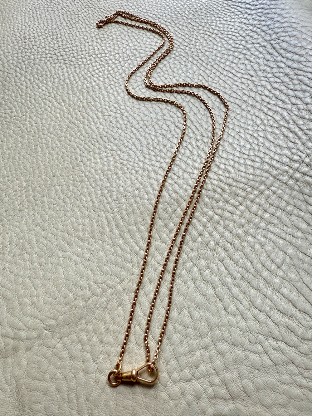 Gold longuard necklace on a textured beige surface