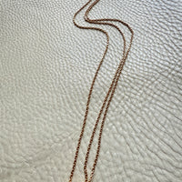 Gold longuard necklace on a textured beige surface